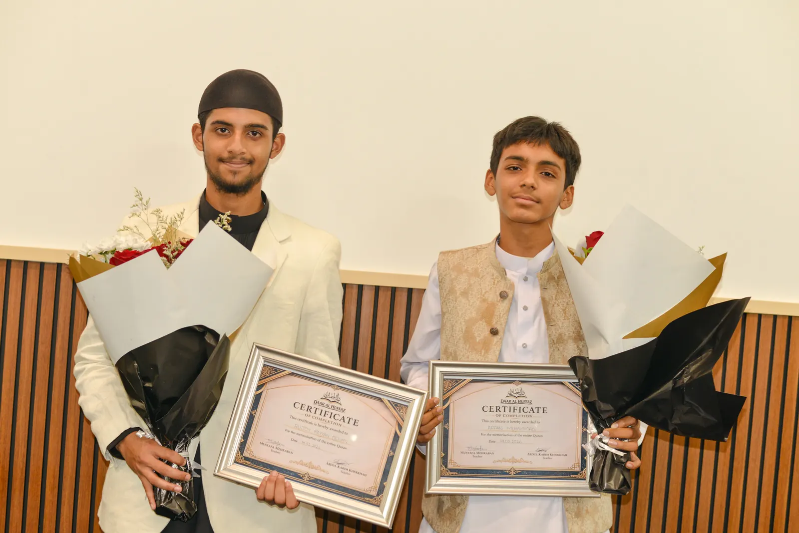 Two graduates holding their certificates and flowers