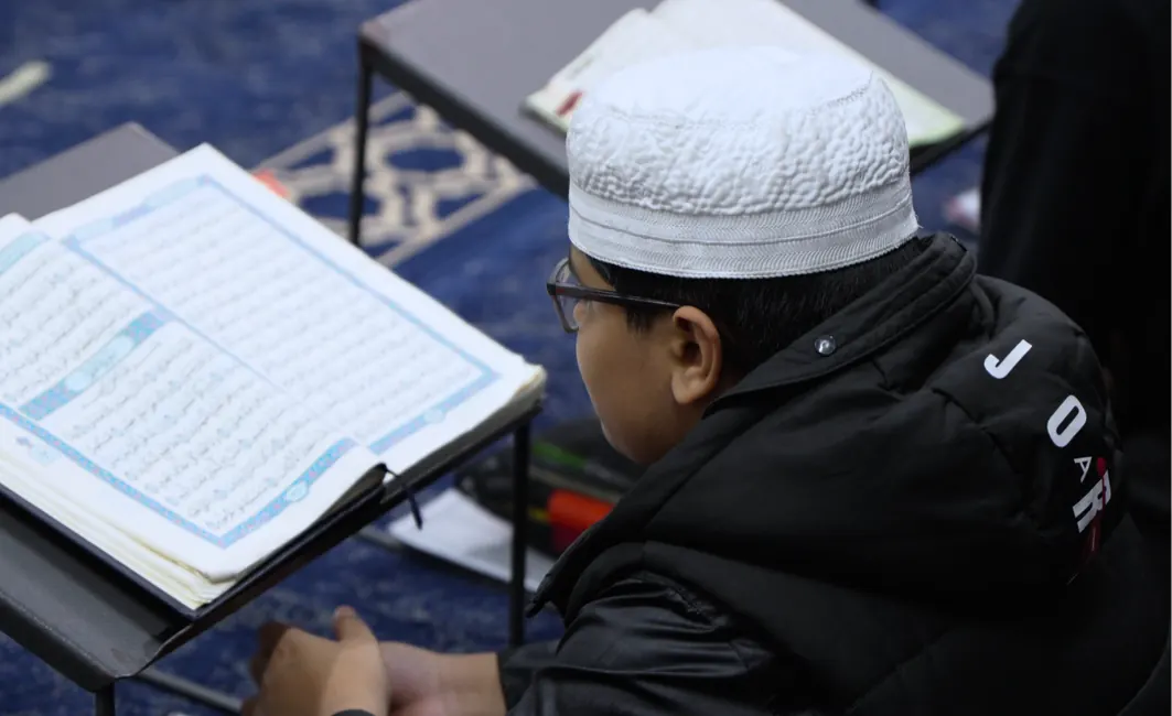 Close-up of a student reading from the Mushaf on a wooden stand