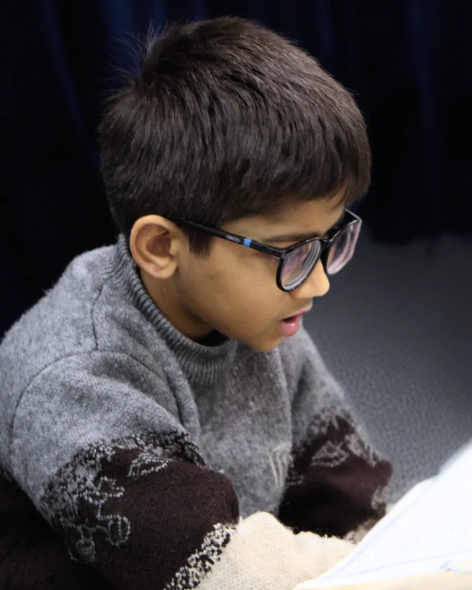 A young boy reading closely from his Mushaf