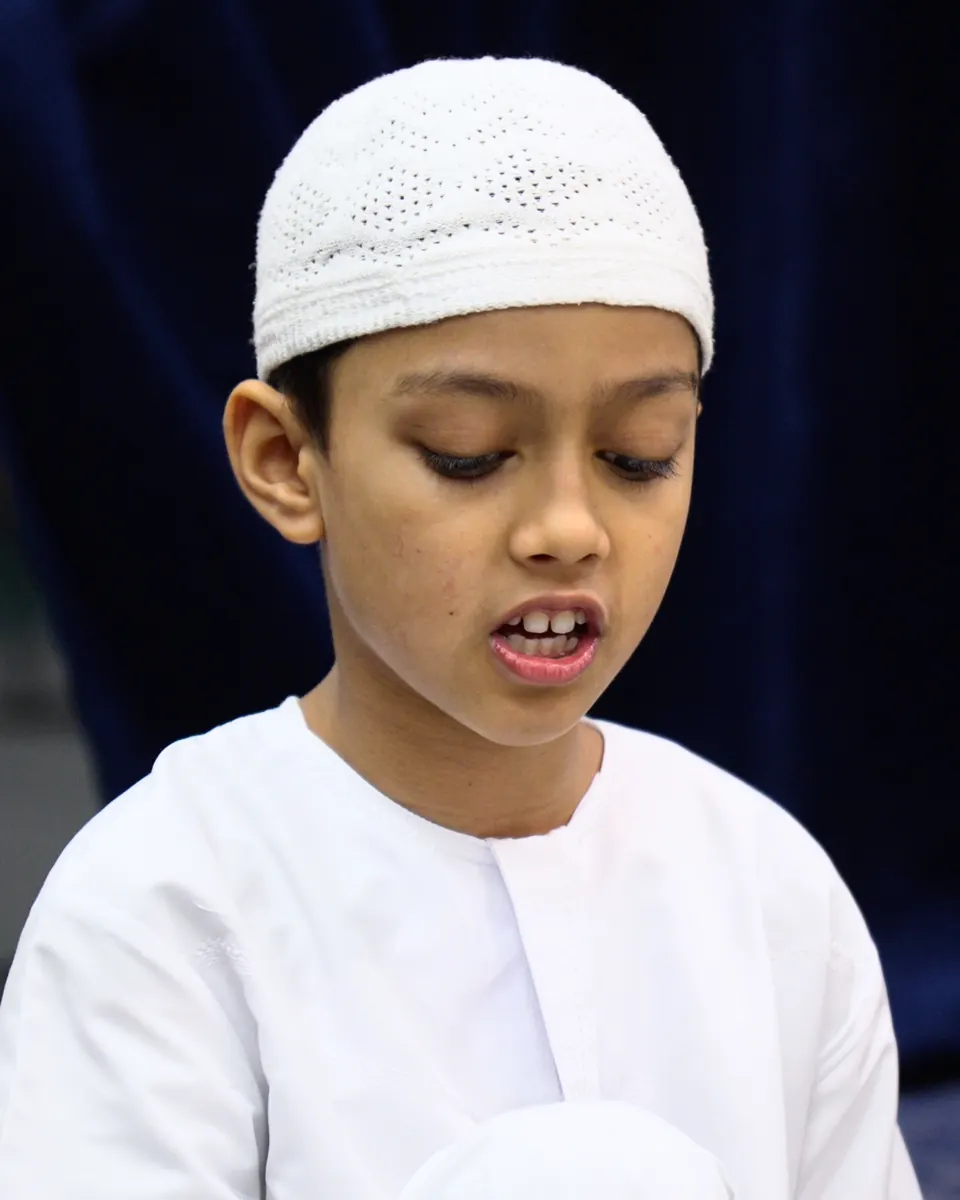 A young student in a white kufi reciting the Qur’an from memory